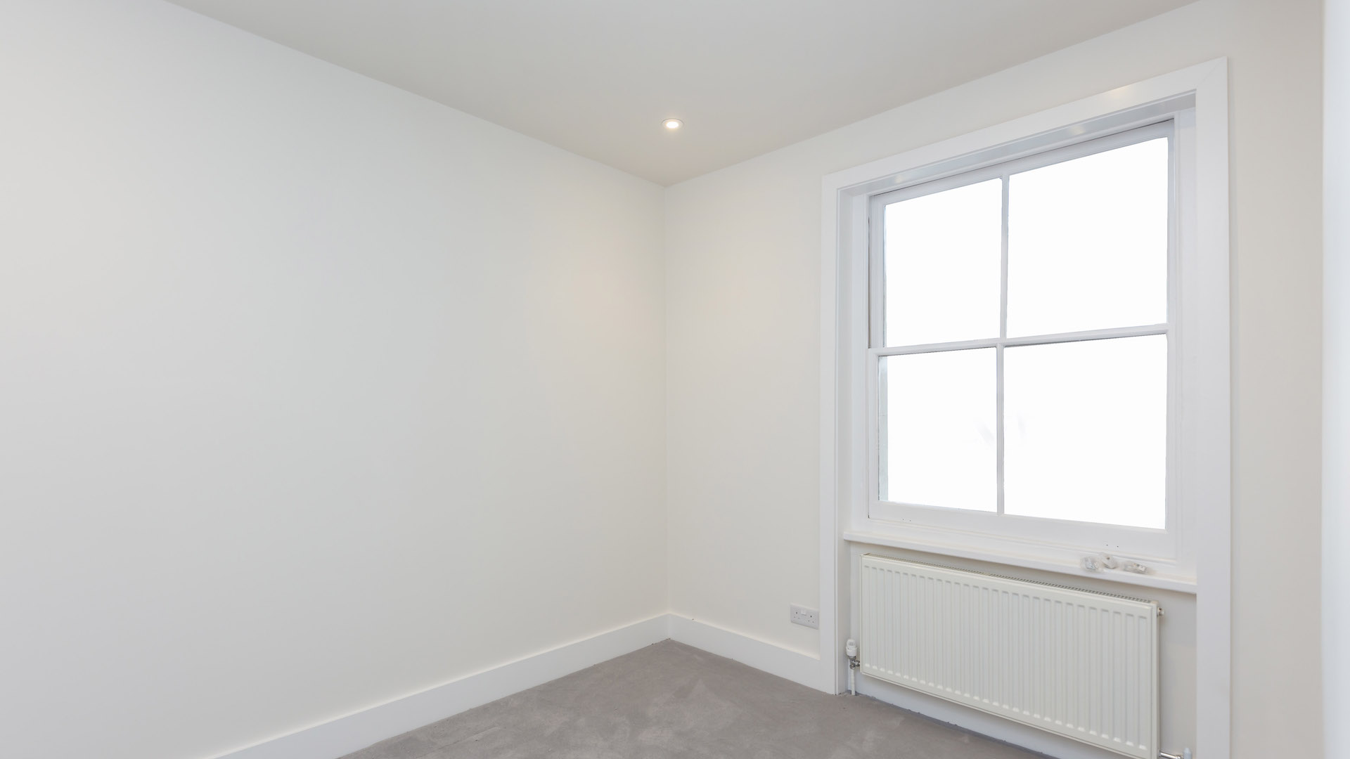 Recently renovated room with off-white walls, heater placed beneath a new window fitting.